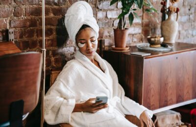 ethnic woman browsing internet on smartphone in beauty salon
