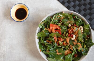 orange edamame salad recipe in a large bowl with a pot of dressing beside it