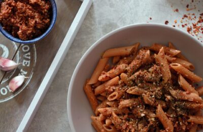 bowl of sundried tomato pesto on pasta with a small pot of pesto beside it