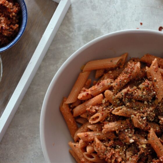 bowl of sundried tomato pesto on pasta with a small pot of pesto beside it