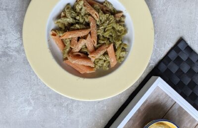 a bowl of olive pesto pasta with a lemon in the top right and a small dish containing pesto in the bottom right of the frame