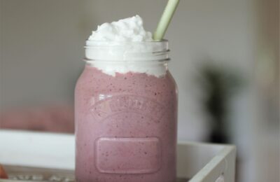 cherry bakwell milkshake recipe in glass jar topped with vegan cream, placed on a wooden tray with a blurred background