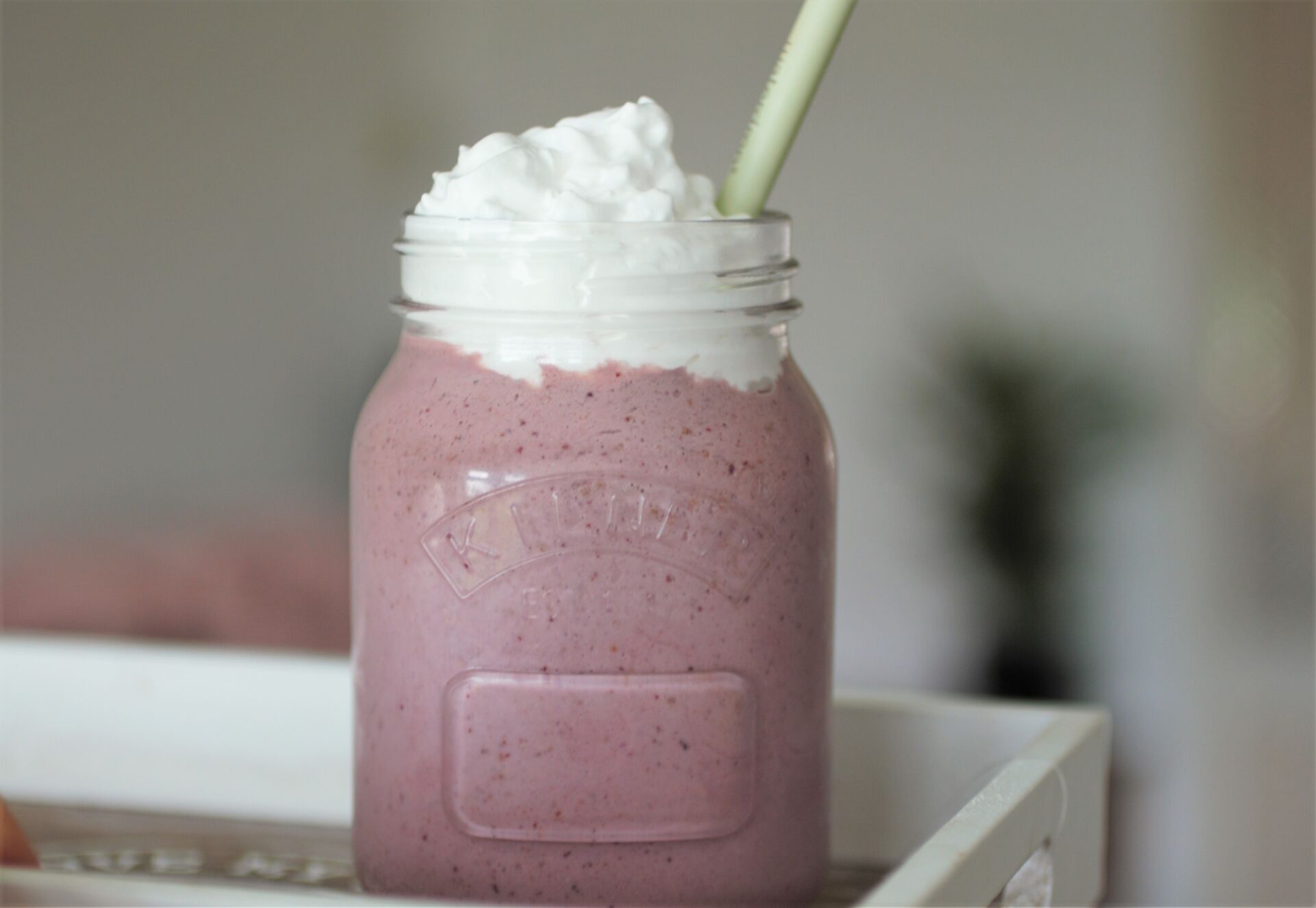 cherry bakwell milkshake recipe in glass jar topped with vegan cream, placed on a wooden tray with a blurred background