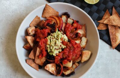 potato burrito bowl recipe against a grey backdrop with tortilla chips and a lime scattered around it