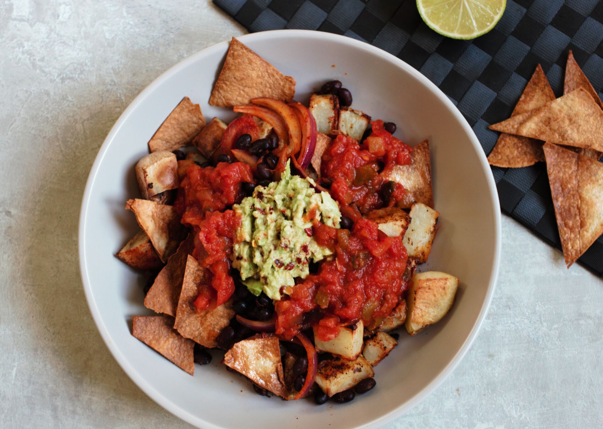 potato burrito bowl recipe against a grey backdrop with tortilla chips and a lime scattered around it