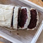 red velvet loaf recipe placed on a wooden board with two freshly cut slices falling to the side