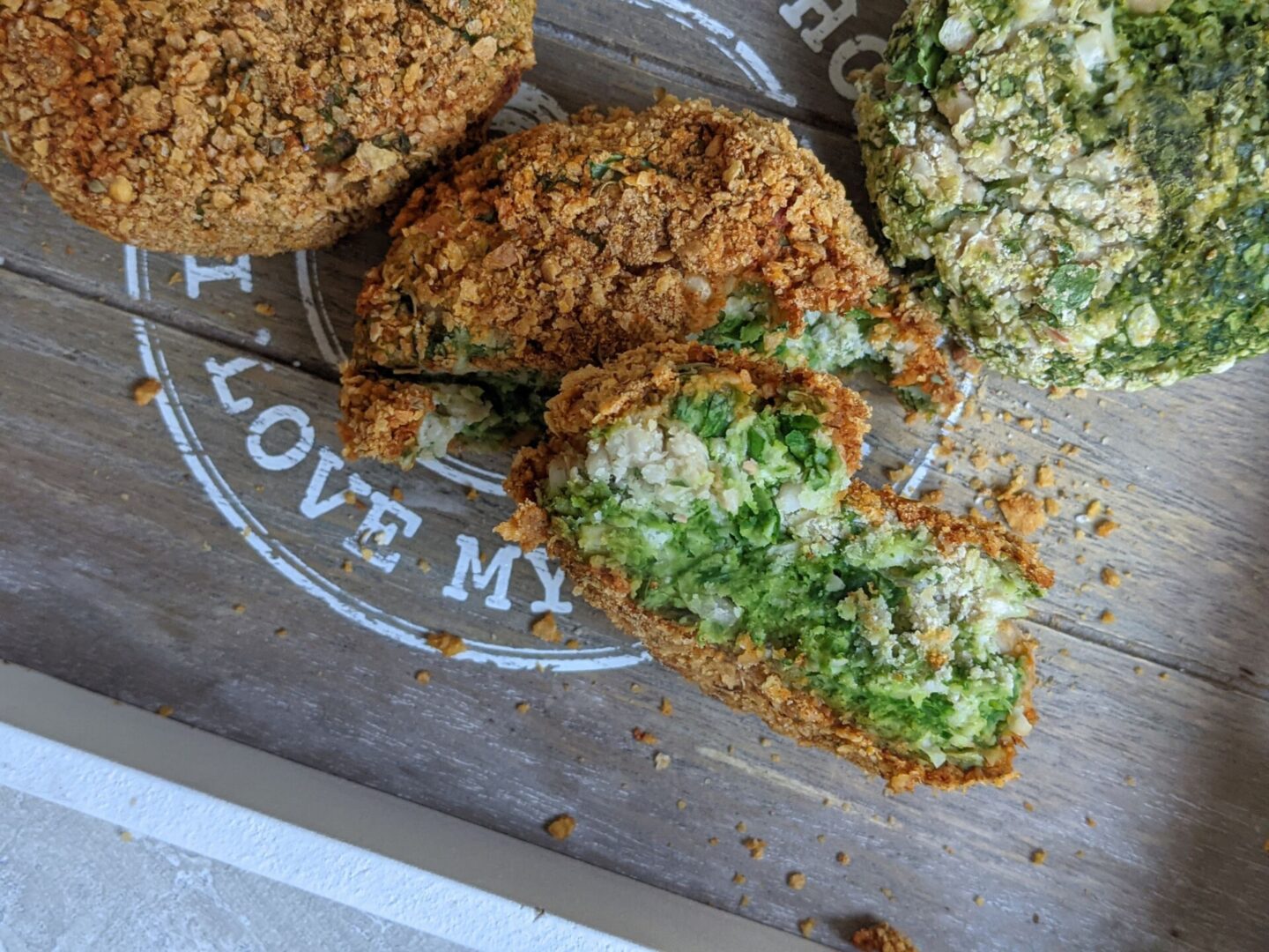 spinach burgers recipe - cooked burger patties on a wooden tray, one broken in half to show the green inside, cooked