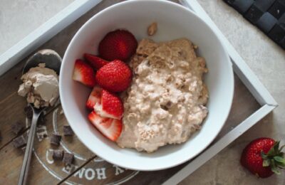 a grey wooden tray with a bowl of cookie dough overnight oats on, with some chopped strawberries