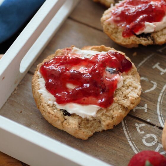 close up shot of a scone on a tray, sliced in half and topped with jam and vegan cream cheese
