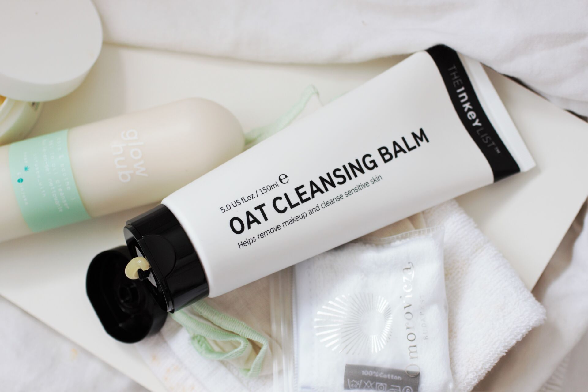 the inkey list oat cleansing balm tube, shot from above with some cloths placed next to it