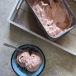 tub of strawberry ice cream recipe next to dish containing two scoops