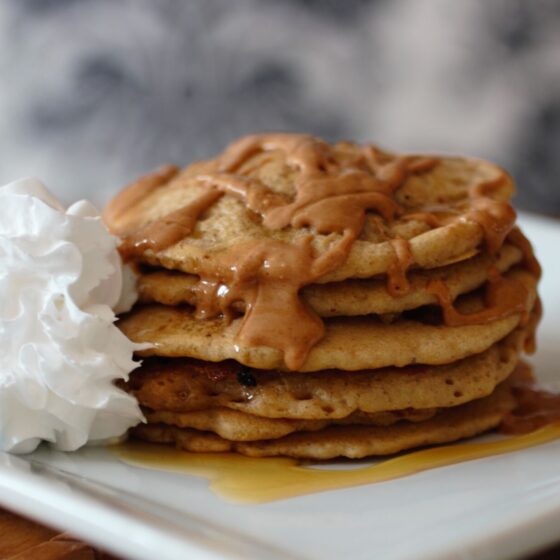birthday breakfast - a stack of pancakes on a white plate with peanut butter and syrup on them