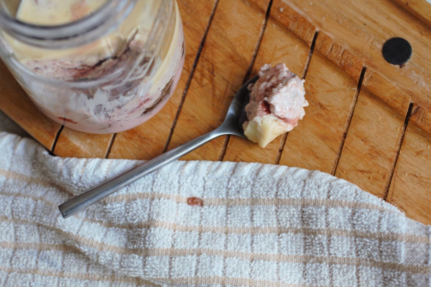a spoon of creamy strawberry cheesecake overnight oats recipe placed next to the kilner jar containing the full recipe