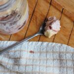 a spoon of creamy strawberry cheesecake overnight oats recipe placed next to the kilner jar containing the full recipe