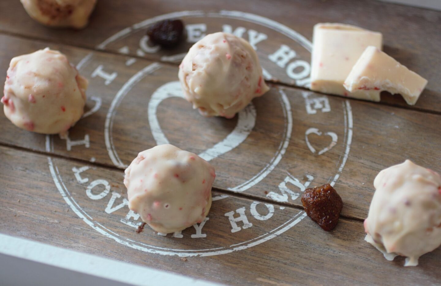 a tray of strawberry white chocolate cheesecake balls with white chocolate and gummy strawberries scattered around