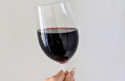 is red wine good for you? - my hand holding a glass of red wine against a plain wall
