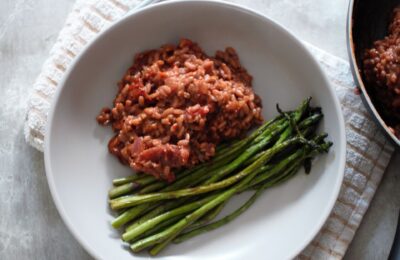 a bowl of red wine risotto with garlic butter asparagus in a stone bowl placed on a neutral check tea towel