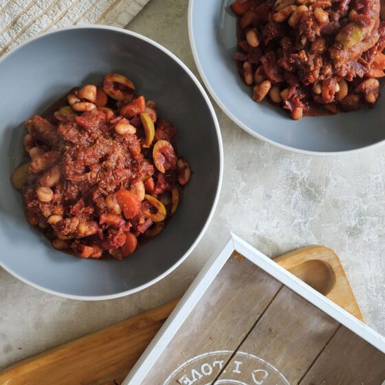 two bowls of vegan sausage & bean casserole against a grey marl background