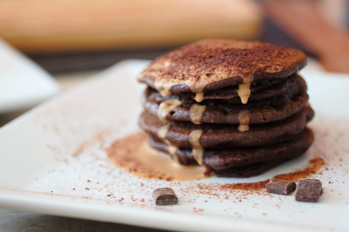 a square white plate with a stack of mocha pancakes and some chocolate chips