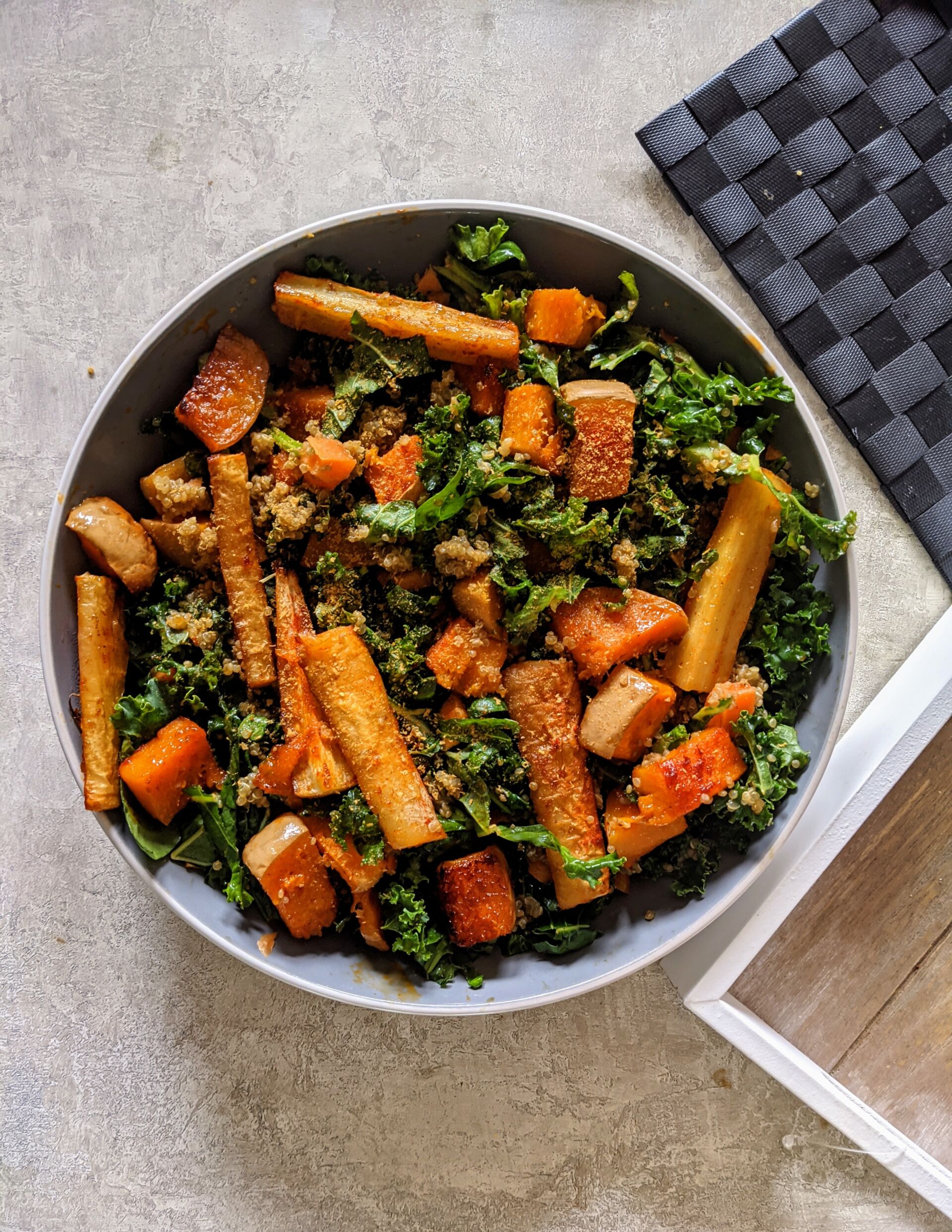 a bowl of fall vegetable salad placed next to a wooden tray