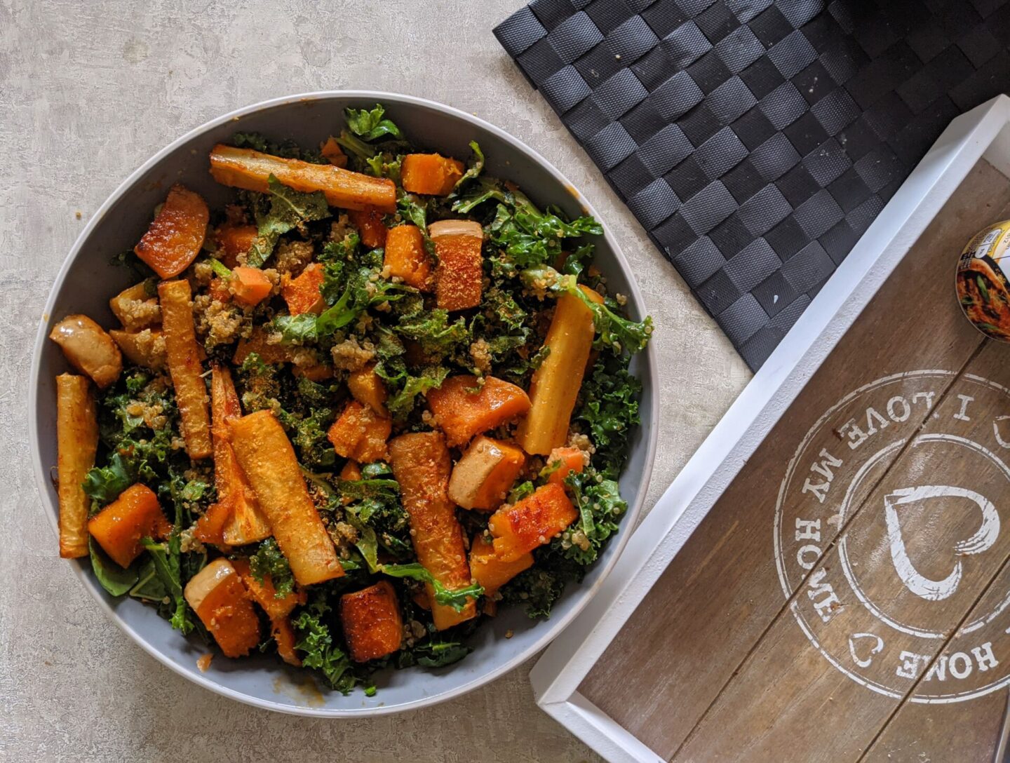 a bowl of fall vegetable salad placed on a dining table with a grey wooden tray and heat mats