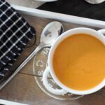 smoked carrot soup recipe in a white bowl placed on a grey wooden tray