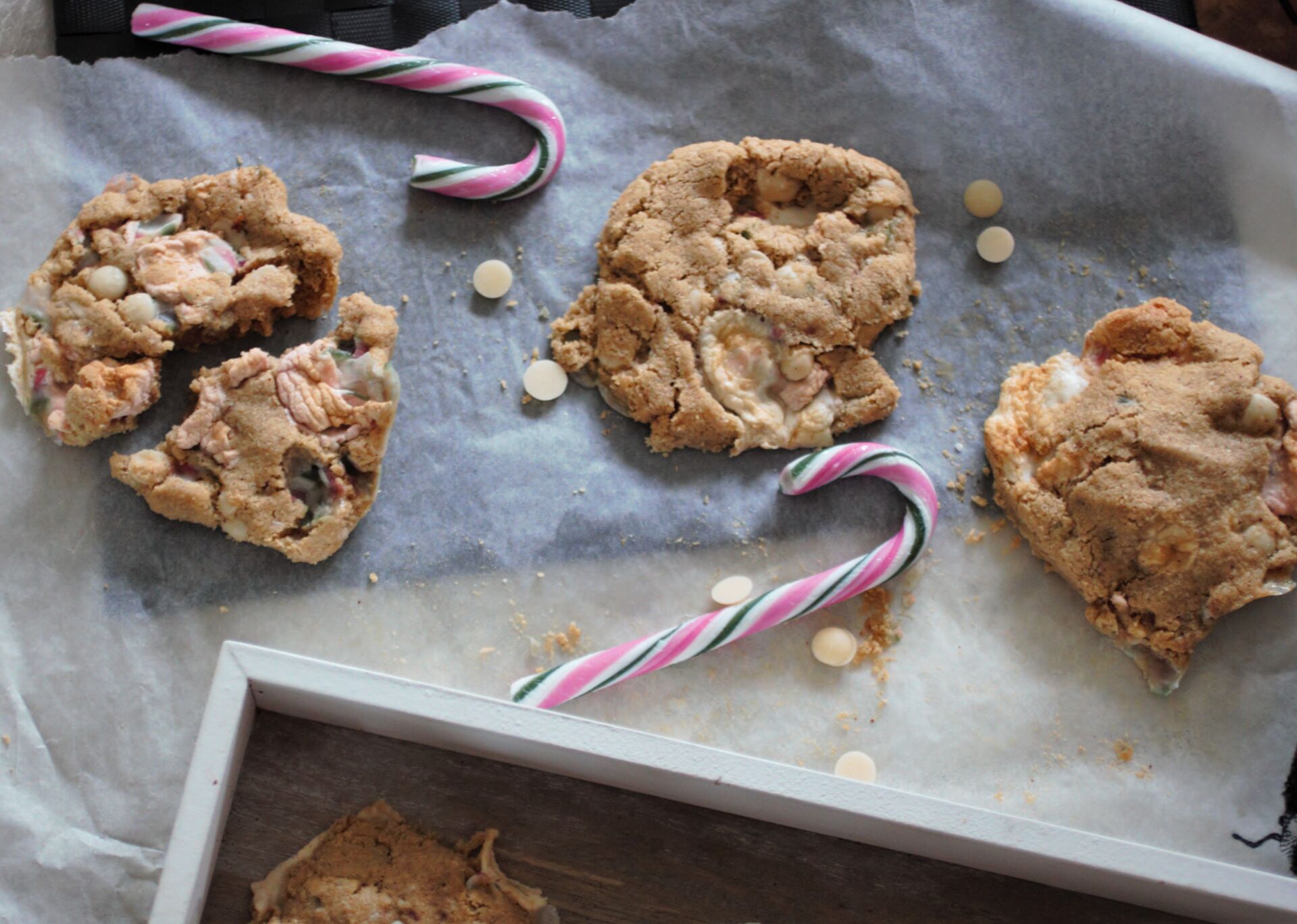 a few candy cane cookies on a sheet of greaseproof paper with candy canes and chocolate chips scattered around them
