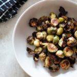 bowl of crispy roasted sprouts with a black and white tea towel placed next to the bowl