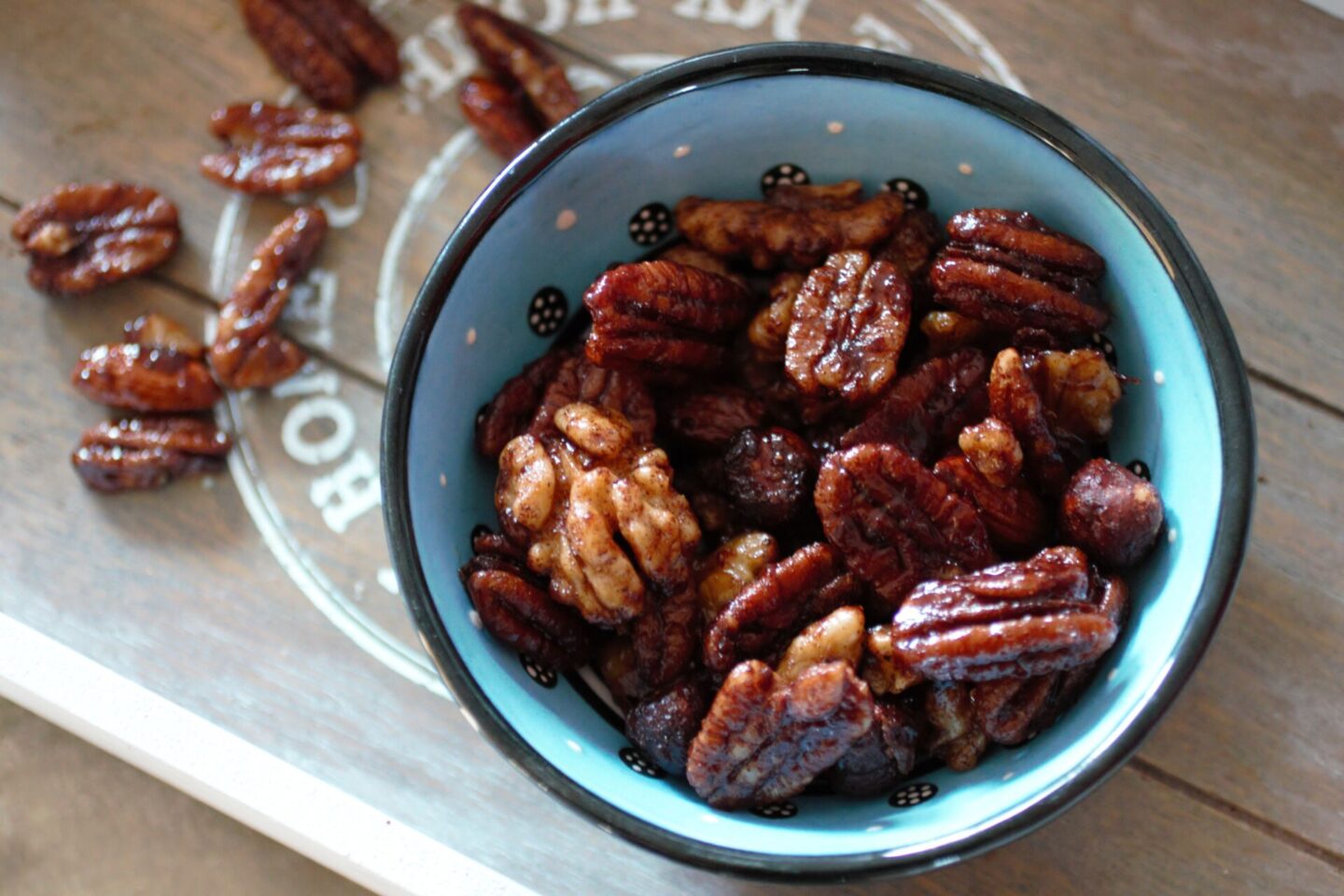 a bowl of the orange candied nuts recipe with a few nuts sprinkled on a wooden tray in the background