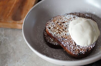 a bowl of orange french toast recipe topped with icing sugar and dairy free yoghurt