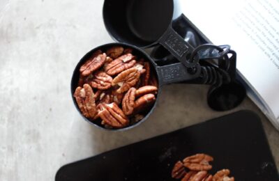 a measuring cup full of nuts placed next to the corner of a cookbook