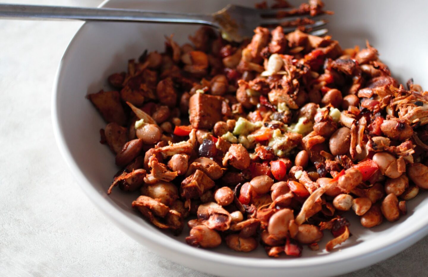 smoky jackfruit recipe in a bowl with pinto beans and guacamole