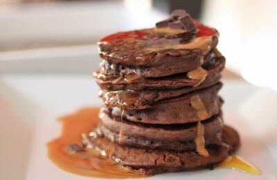stack of peanut chocolate pancakes recipe topped with syrup, on a white plate