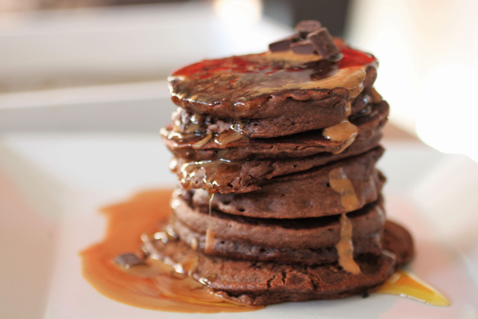 stack of peanut chocolate pancakes recipe topped with syrup, on a white plate