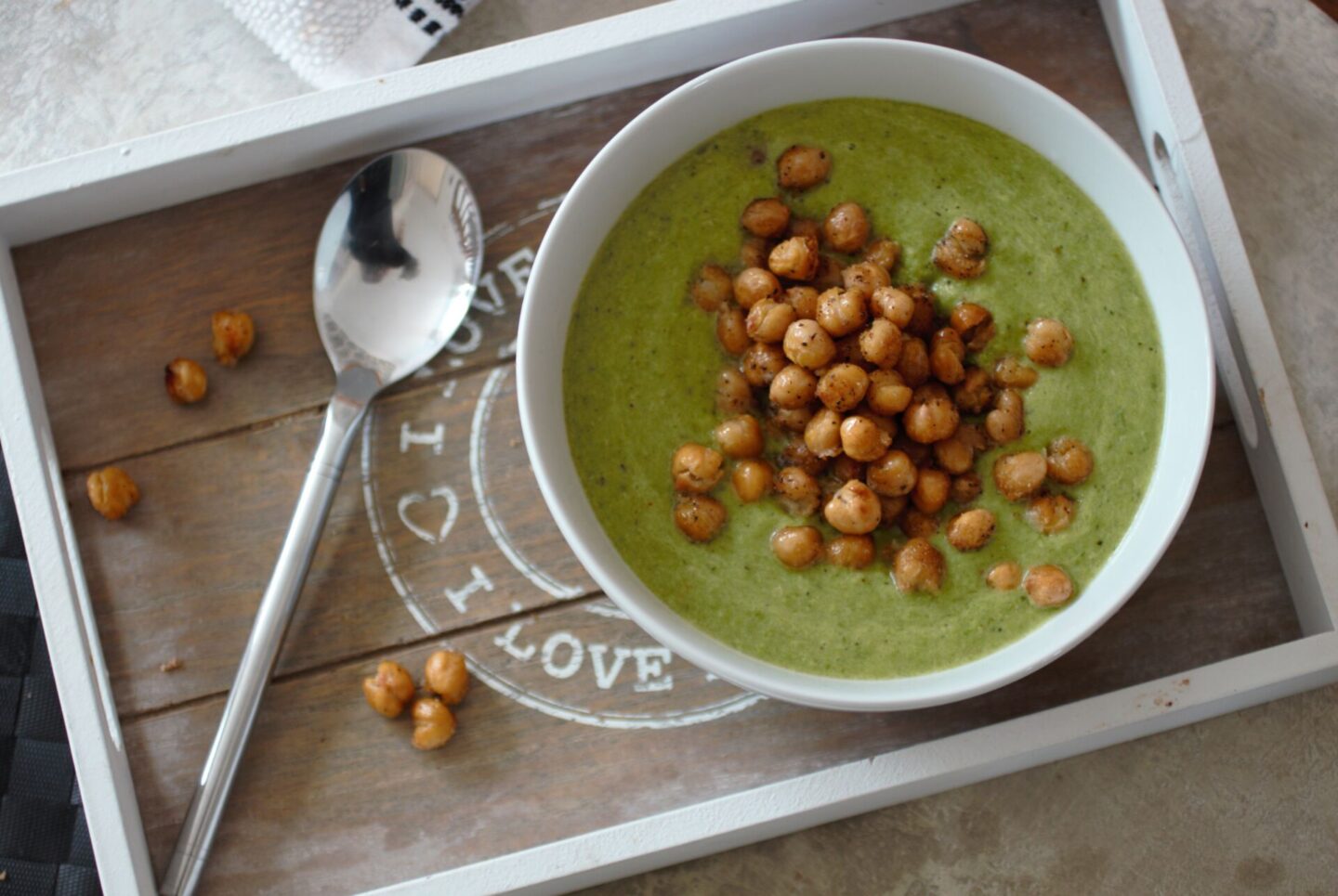 bowl of asparagus & pea soup recipe topped with roasted chickpeas, placed on a wooden tray, shot from above