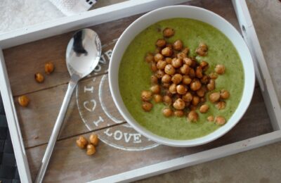 bowl of asparagus & pea soup recipe topped with roasted chickpeas, placed on a wooden tray, shot from above