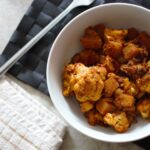 a bowl of aloo gobi placed on a black place mat, next to a tea towel
