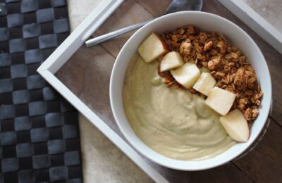 apple pie smoothie bowl in a white bowl, topped with fresh apples and granola, shot from above