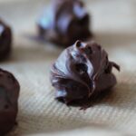 a close up of one vegan chocolate truffle on a sheet of baking paper
