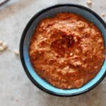 a small blue dish filled with red pepper pesto with chilli flakes and pine nuts sprinkled around it