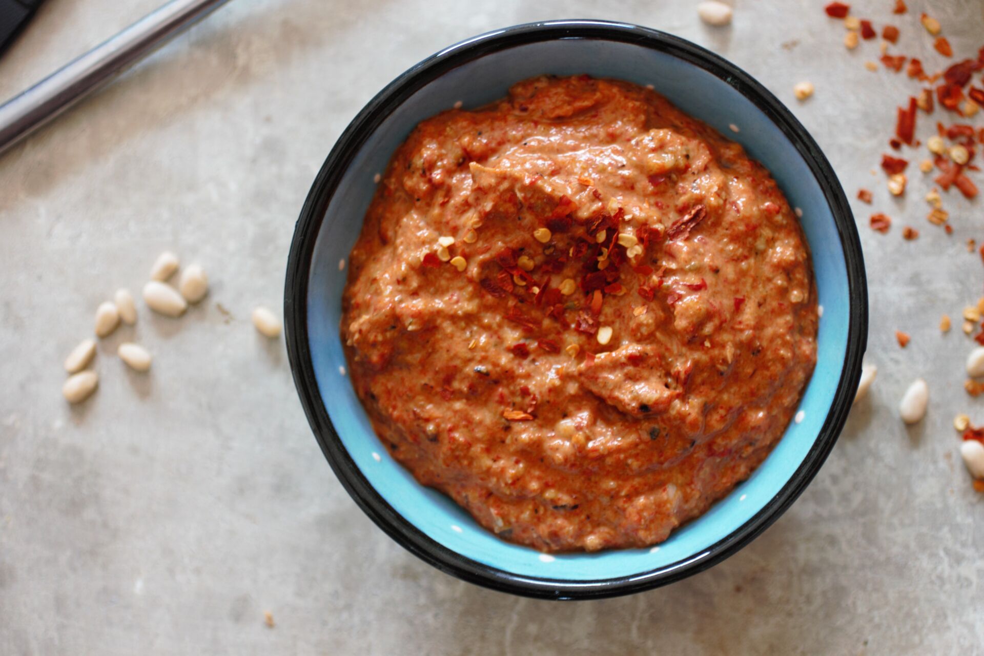 a small blue dish filled with red pepper pesto with chilli flakes and pine nuts sprinkled around it
