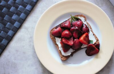 balsamic strawberry toast on a white and yellow plate against a grey marl background