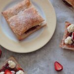 a strawberry cream puff on a plate with some others half assembled scattered around it