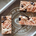 a grey wooden tray with strawberry white chocolate rice krispy treats on it