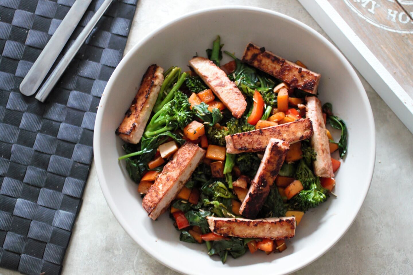 light grey bowl filled with tofu summer salad recipe, against a grey marl backdrop and a black placemat