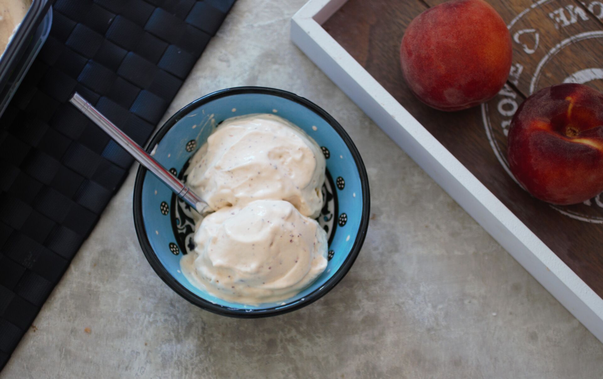 2 scoops of vegan peach ice cream recipe in a blue bowl next to a tray with peaches on