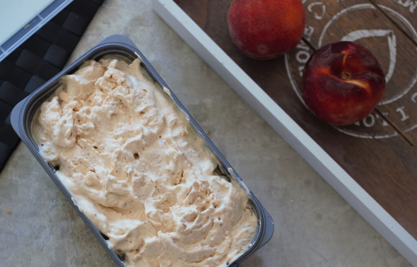 tub of vegan peach ice cream on a table next to some peaches