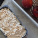tub of vegan peach ice cream on a table next to some peaches