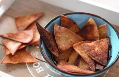 small blue ceramic dish filled with maple bacon tortilla chips with some more scattered on the surrounding area