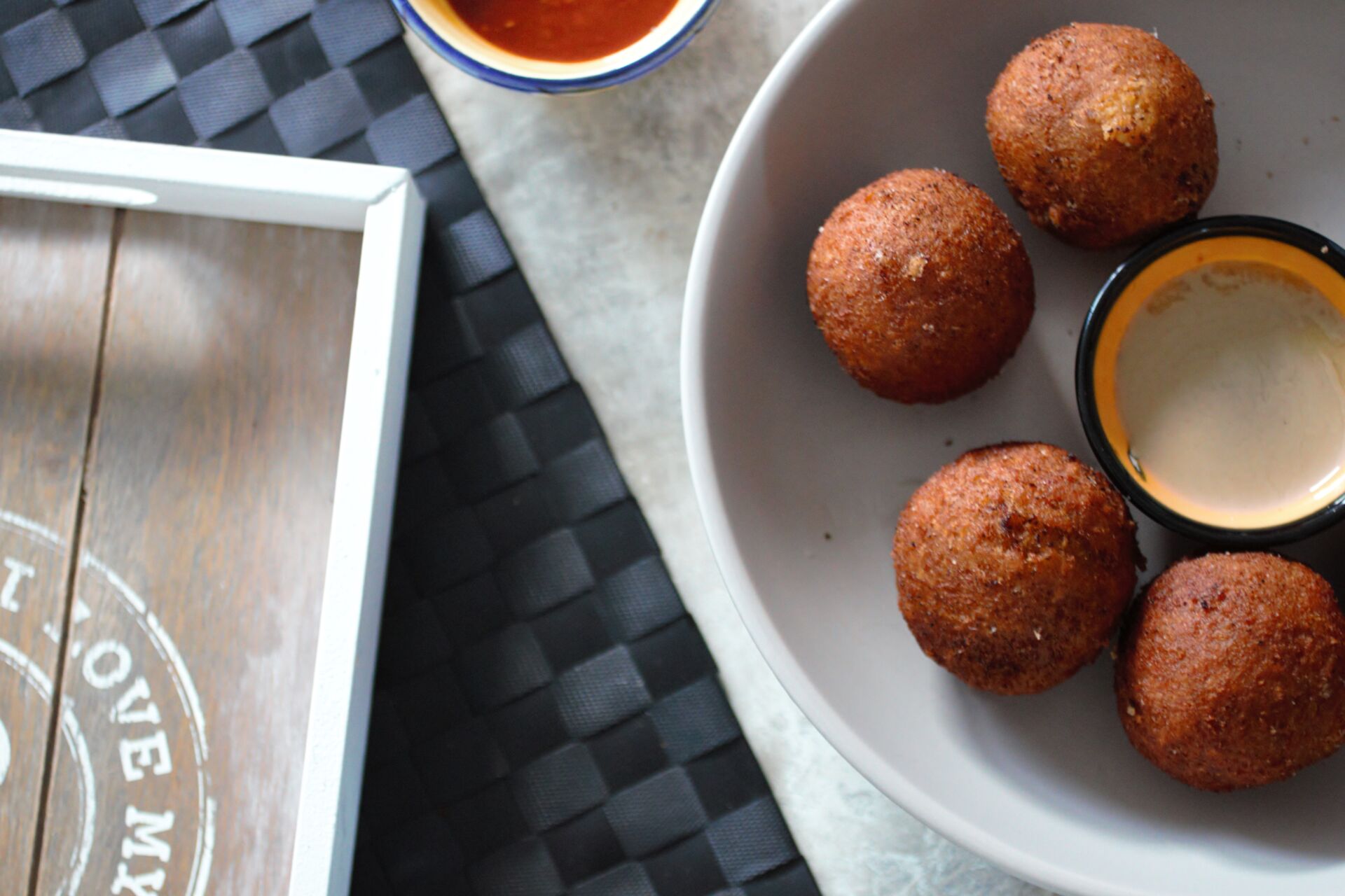 a bowl of pumpkin falafel with a pot of tahini and hot sauce